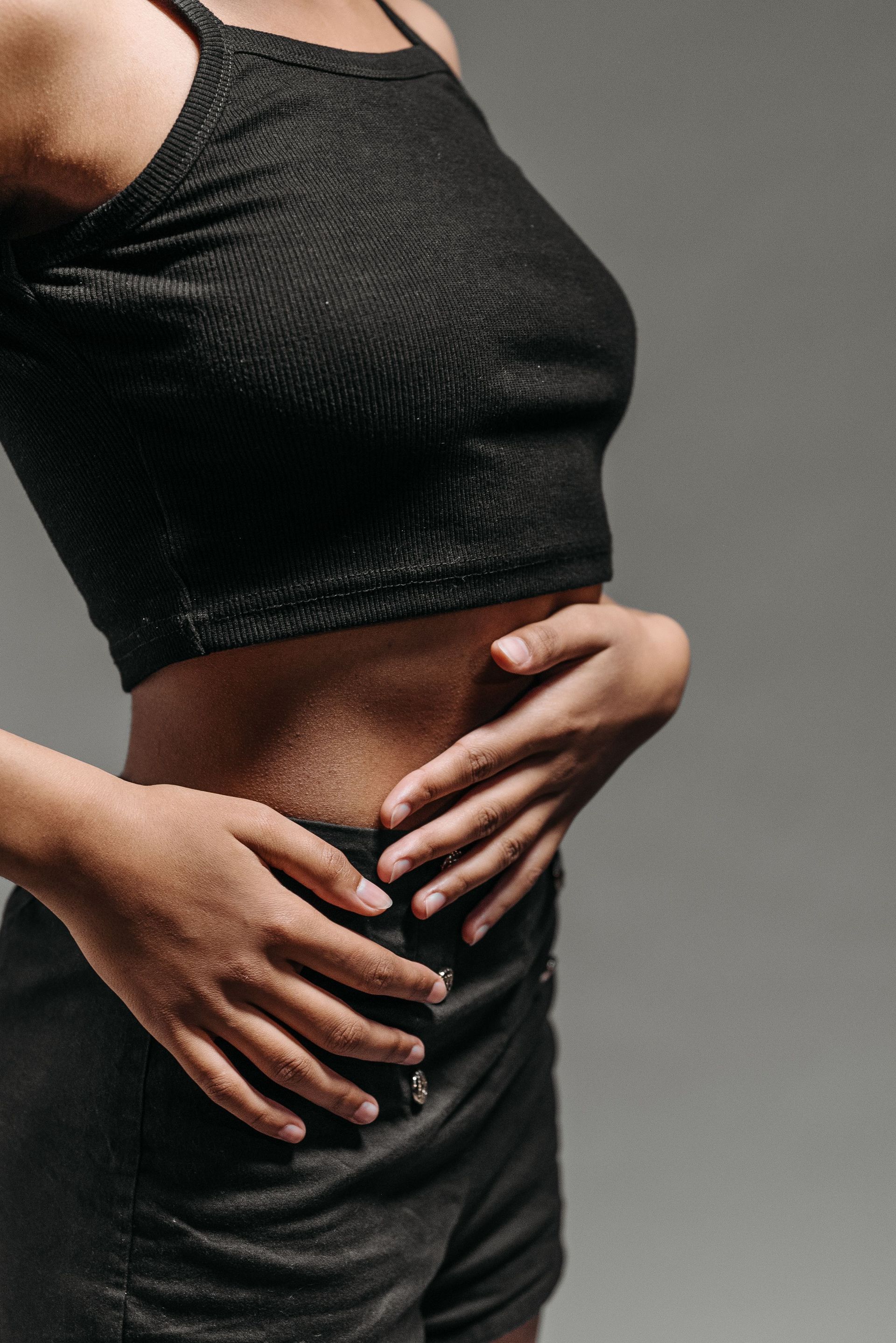 Close-up of a woman wearing a casual black outfit indoors, highlighting her torso and hands.