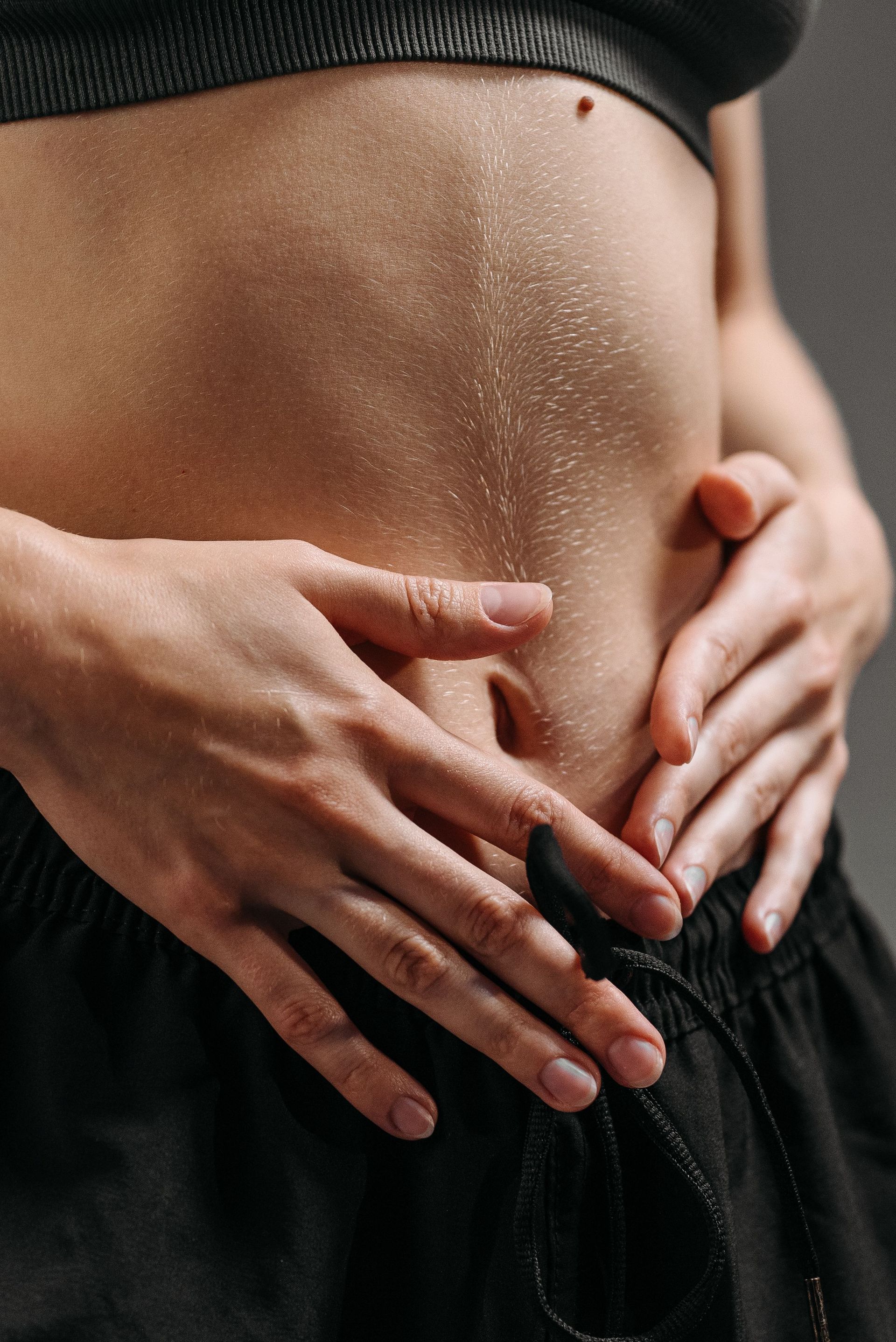 Hands resting on a toned stomach in sportswear, reflecting fitness and health.