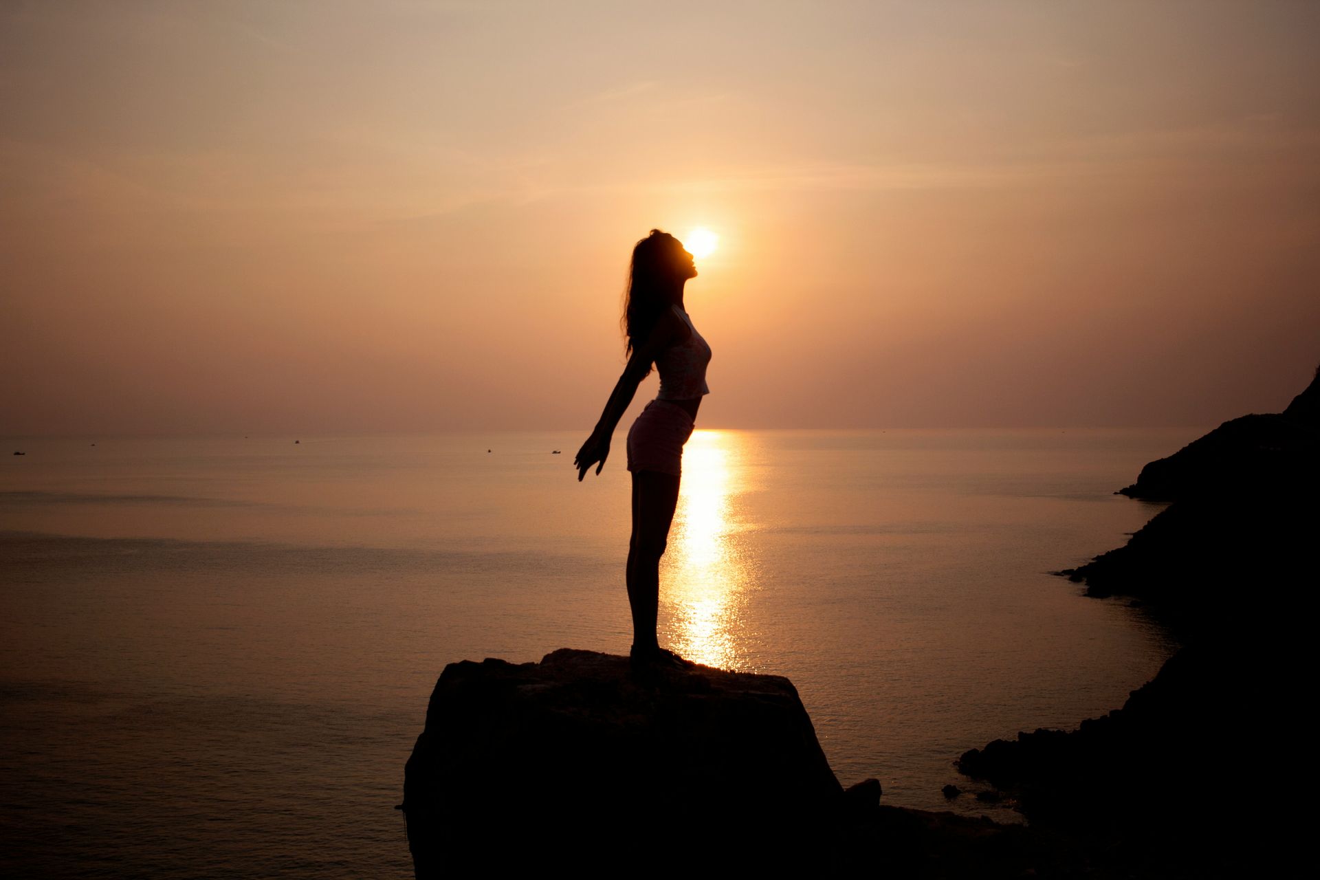 silhouette of woman standing on sea cliff during golden hour